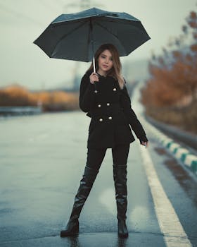 Chic woman dressed in fashionable attire holding an umbrella on a rainy street.