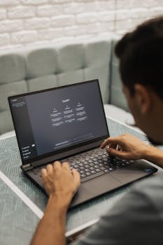 A man types on a laptop running AI software, seated in a modern indoor setting.