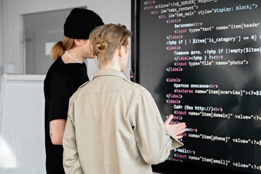 Two developers examining code on a large screen in a modern office space, focusing on web development.