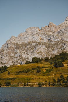 A stunning rocky mountain landscape with a tranquil lake and lush greenery under a clear blue sky.