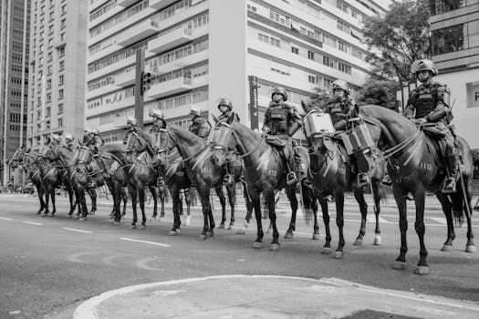 Black and white image of mounted police officers patrolling a street in São Paulo, Brazil, highlighting urban security.