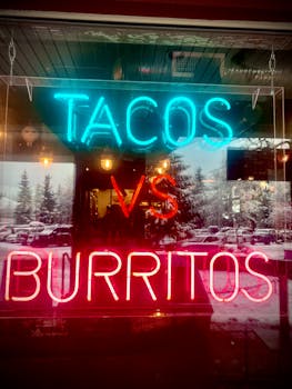 Eye-catching neon sign highlighting tacos vs burritos debate in a shop window with snowy reflections.